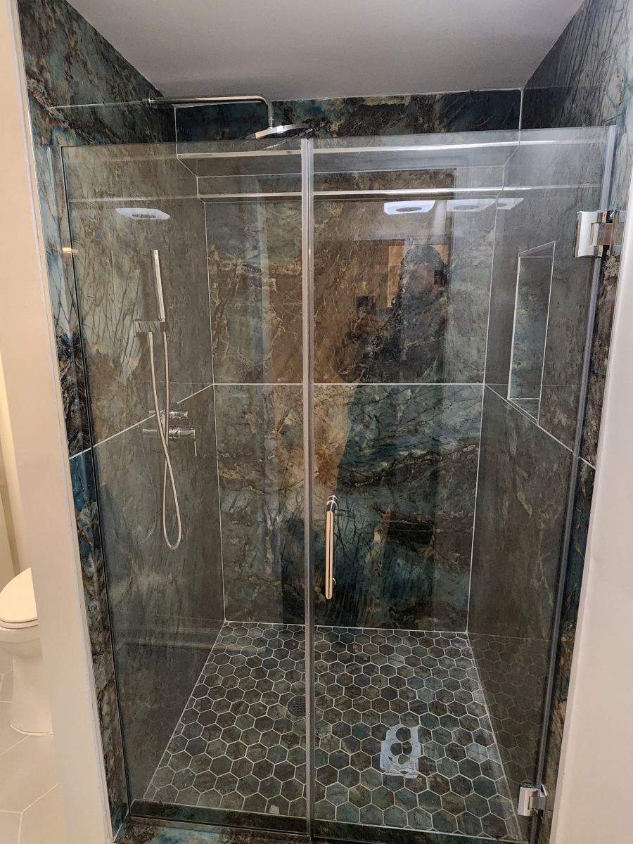 Shower stall with glass doors and textured, blue-green tile. Pebble tile flooring.