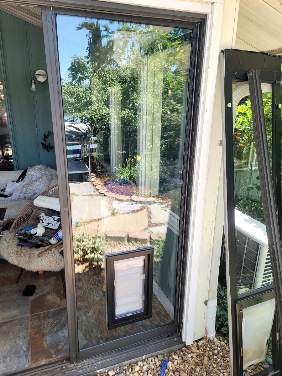 Sliding glass door frame with a pet door installed, leaned against a house.