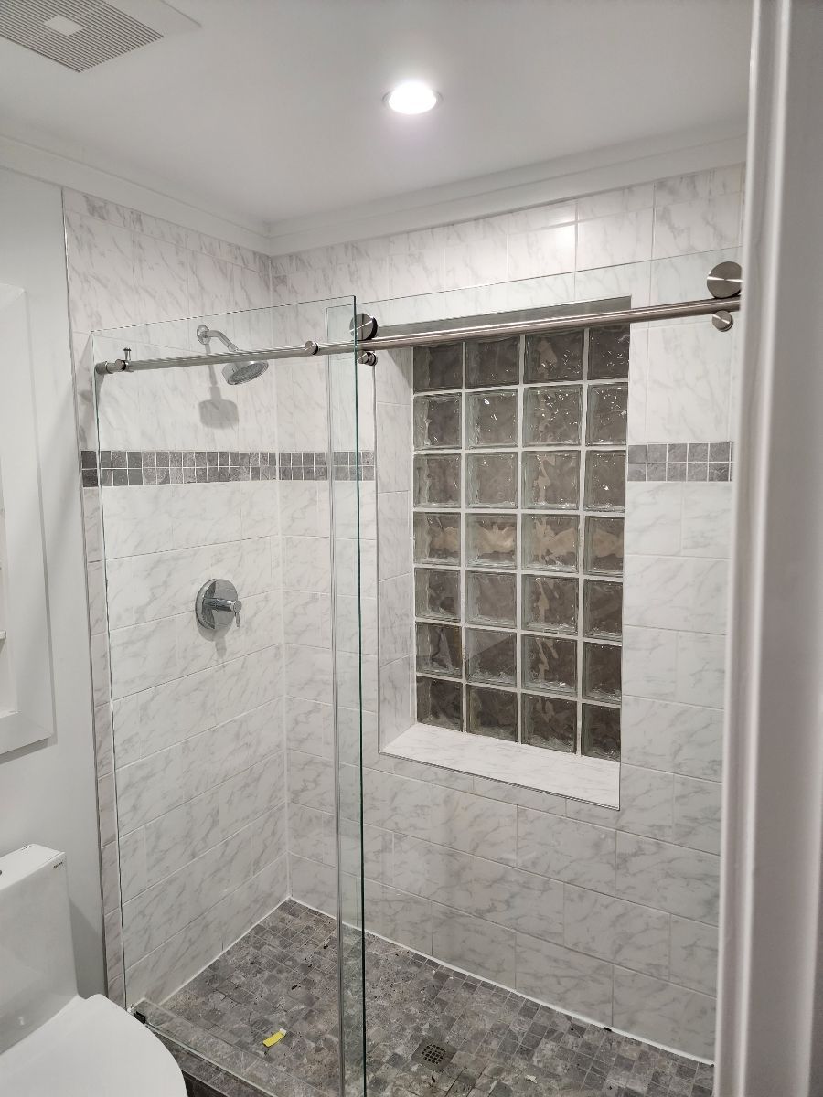Shower with sliding glass door, white and gray tile, built-in shelf with glass blocks.