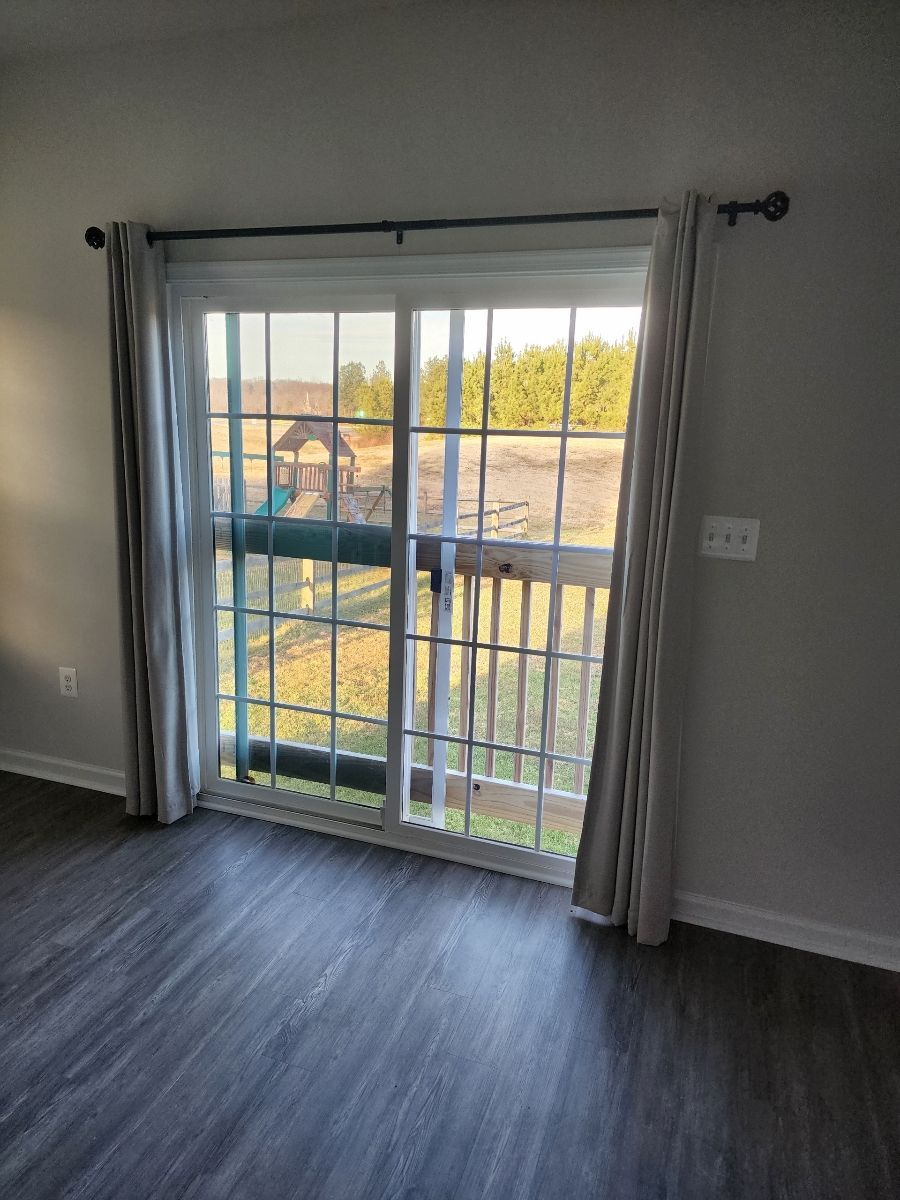 Sliding glass door with light gray curtains, looking out to a deck, and a playground.