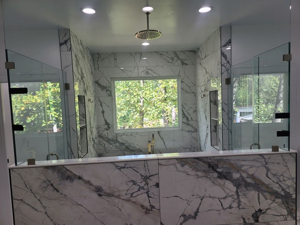 A bathroom with marble walls , a tub , a shower and a window.