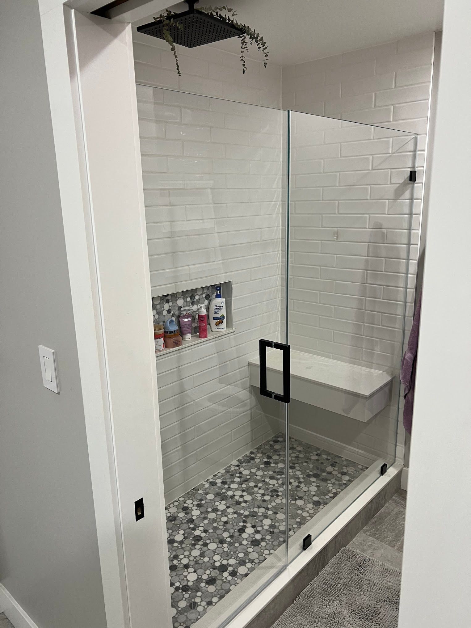 A bathroom with a walk in shower with a glass door and a bench.