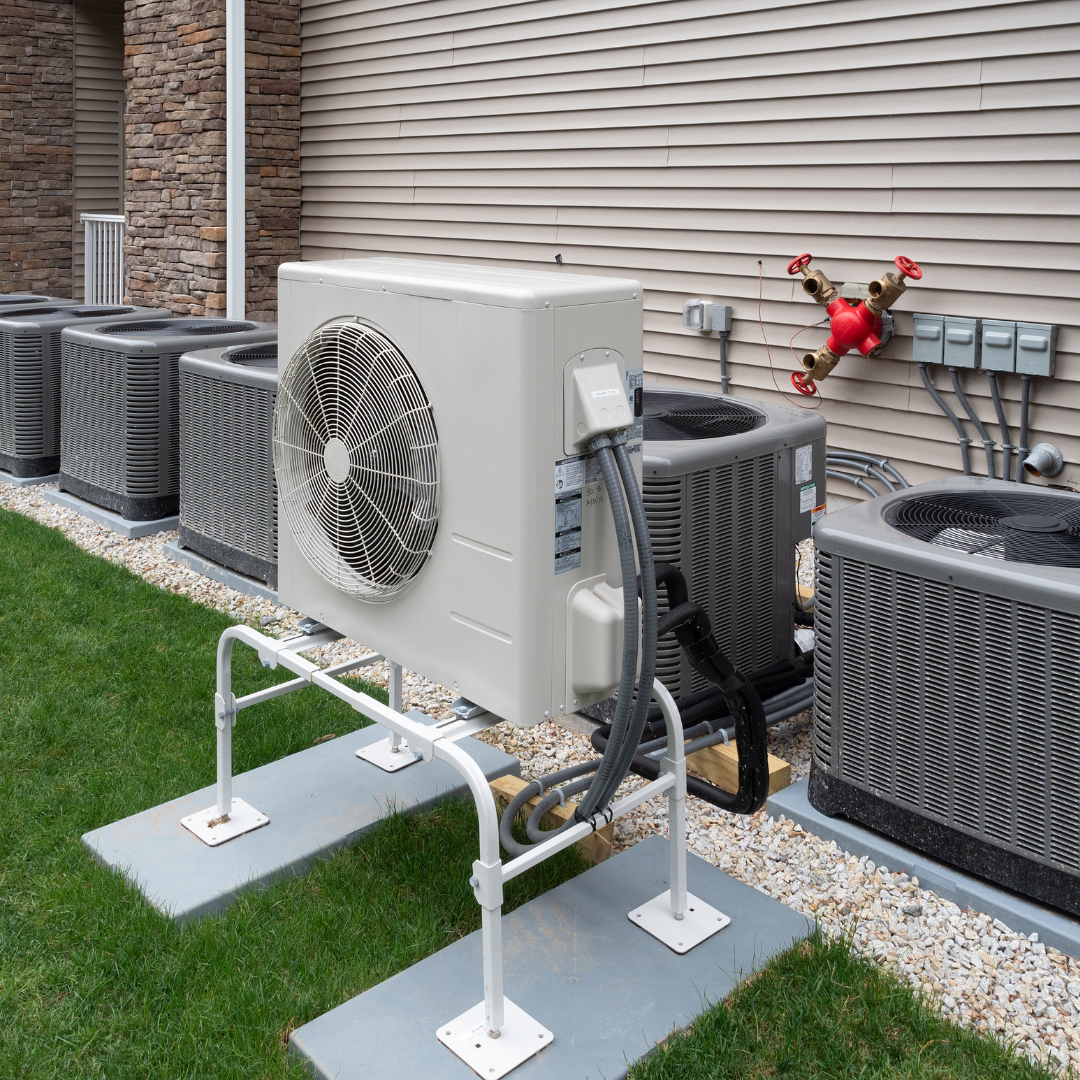 A row of air conditioners are sitting outside of a house.