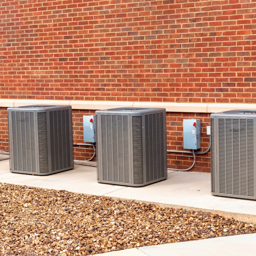 Three air conditioners are sitting outside of a brick building.