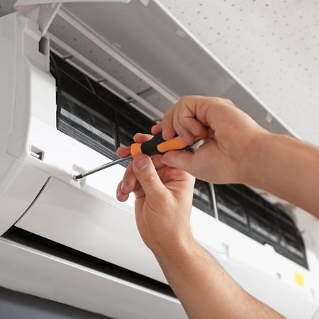 A person is fixing an air conditioner with a screwdriver