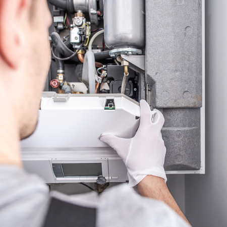 A man wearing white gloves is working on a boiler.