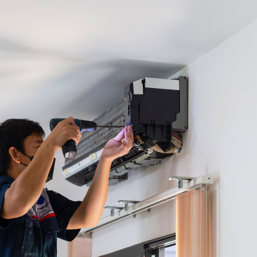 A man is fixing an air conditioner with a drill.