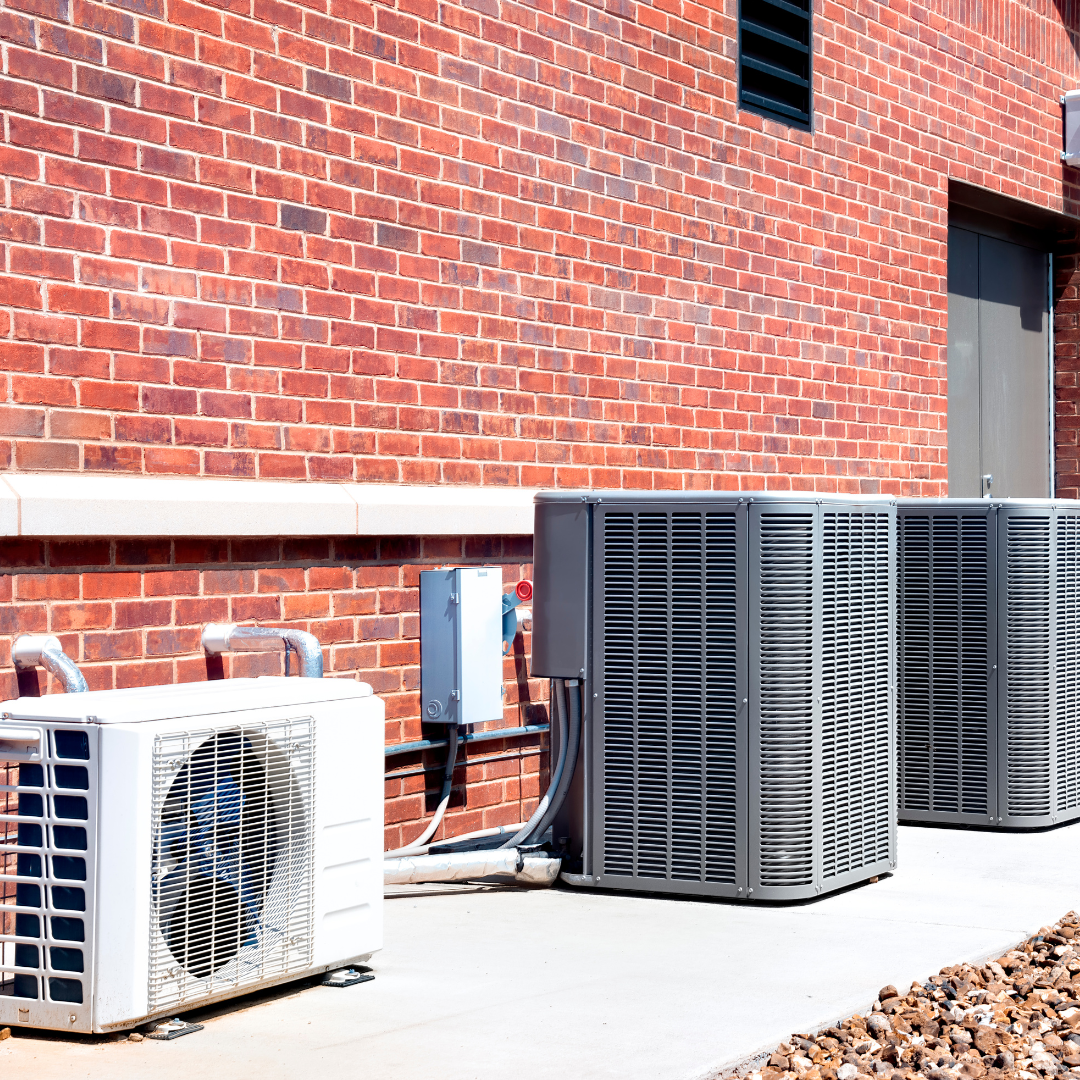 Two air conditioners are sitting outside of a brick building