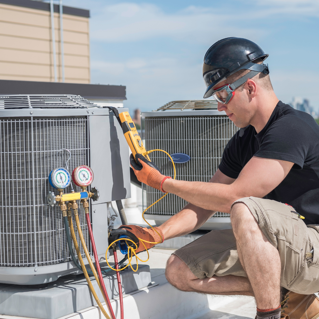 A man is working on an air conditioner on the roof of a building.