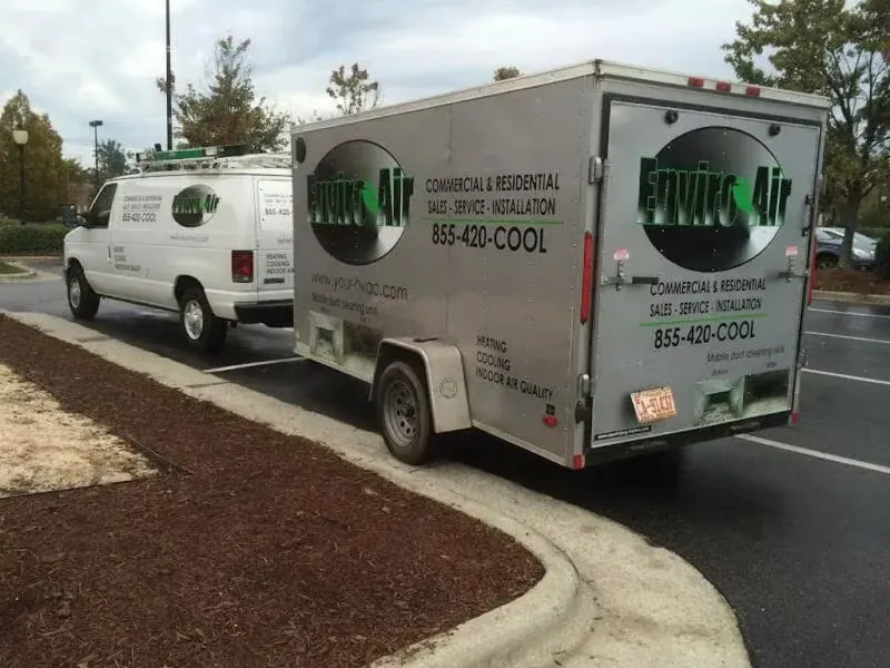 Two vans and a trailer are parked on the side of the road.