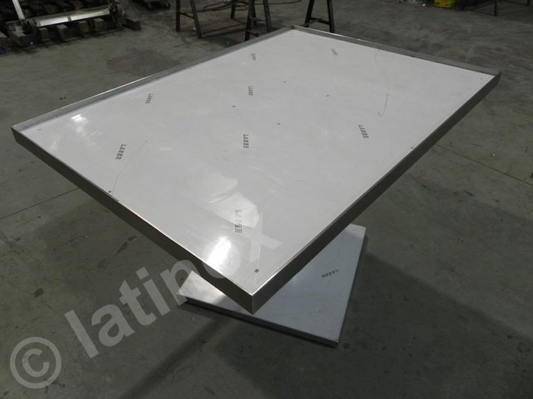 Tavolo moderno in acciaio inox con piano rettangolare e base angolare in un'officina.