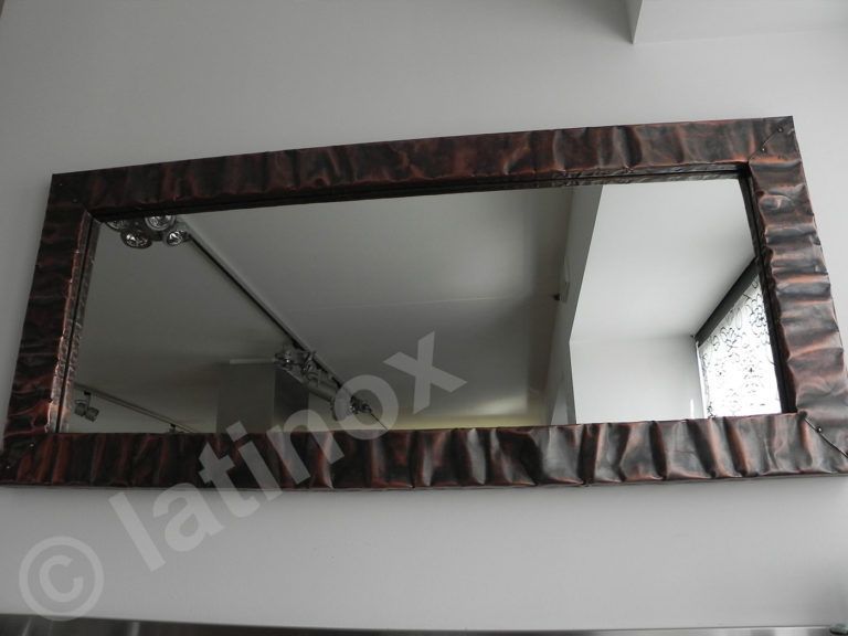 Specchio rettangolare con cornice testurizzata color rame, montato su una parete bianca.