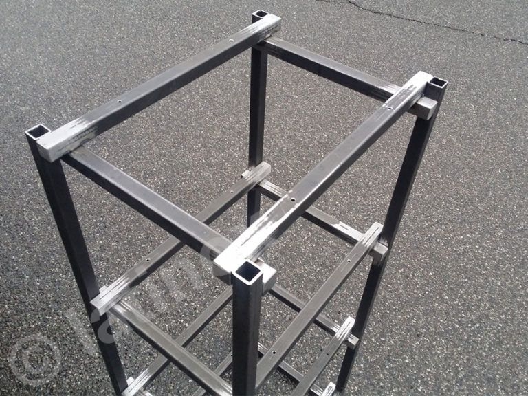 Struttura metallica a telaio quadrato, composta da pali verticali e supporti orizzontali, su una superficie asfaltata.