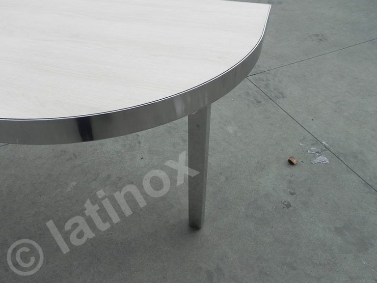 Primo piano di un tavolo semicircolare in acciaio inossidabile con bordo arrotondato e due gambe su una superficie di cemento.