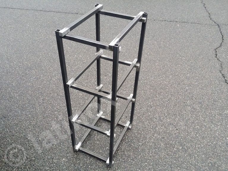 Scaffale portaoggetti in metallo nero con quattro ripiani rettangolari su pavimento grigio.