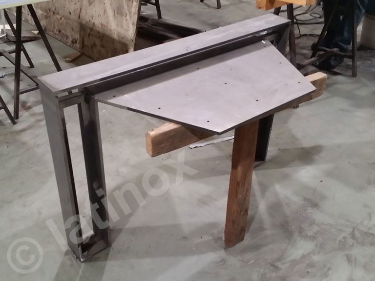 Tavolo da lavoro in metallo con piano inclinato, sostenuto da una struttura in legno e acciaio.