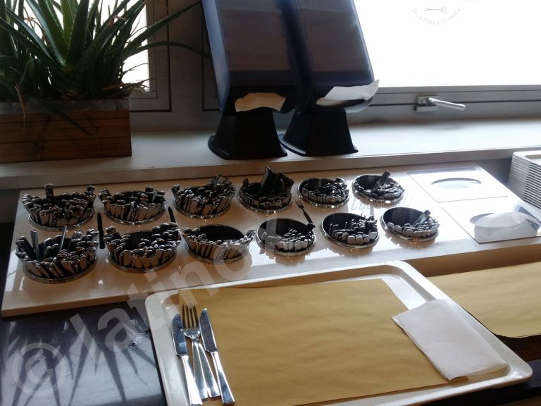 Allestimento del buffet: vassoi di posate, tovaglioli e piccole ciotole di cibo, vicino a una finestra.