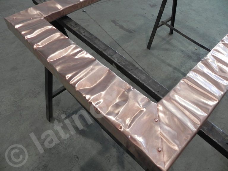 Cornice in rame con superficie strutturata e angoli rivettati su un banco da lavoro.