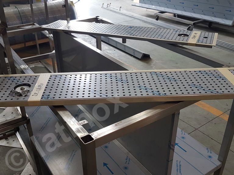 Area di lavoro in metallo con superfici in acciaio perforato e telai di supporto.