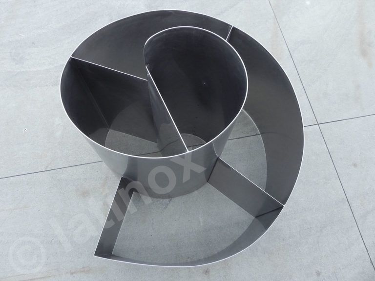 Contenitore metallico nero a forma di spirale, diviso in quattro sezioni, su una superficie di colore chiaro.