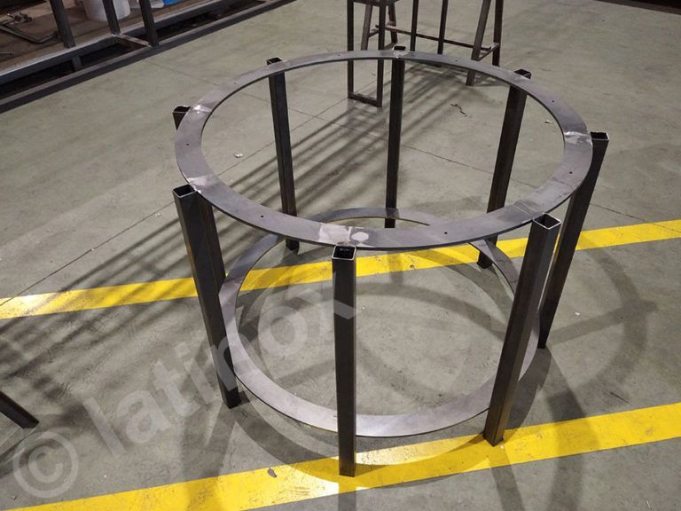 Struttura del tavolo in metallo: piano e fondo circolari con supporti verticali, su pavimento di fabbrica.