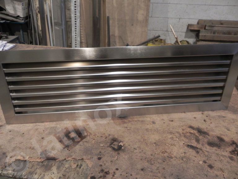 Bocchetta in acciaio inox con lamelle orizzontali, appoggiata su una superficie in legno.