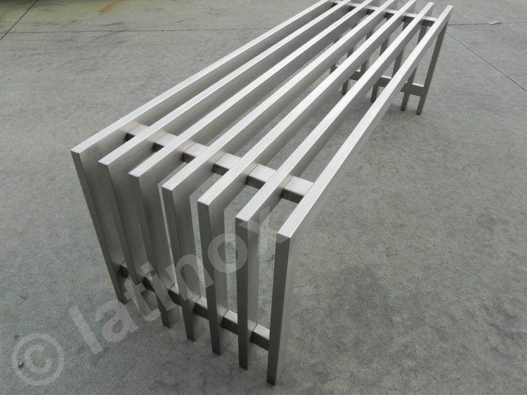 Panca in metallo con doghe verticali e gambe di supporto su superficie in cemento.