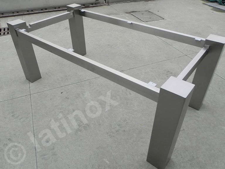 Struttura del tavolo in metallo con quattro gambe quadrate e travi di supporto rettangolari su una superficie in cemento.