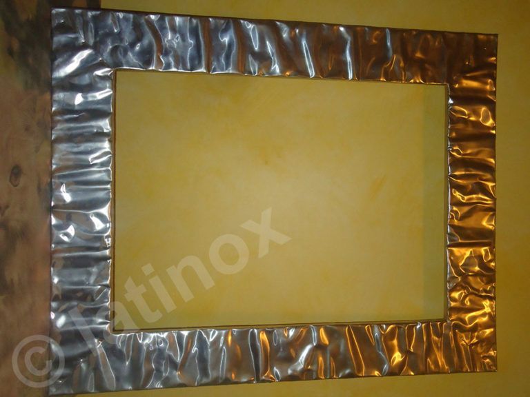 Cornice rivestita in lamina d'argento con centro giallo, montata su una parete gialla.