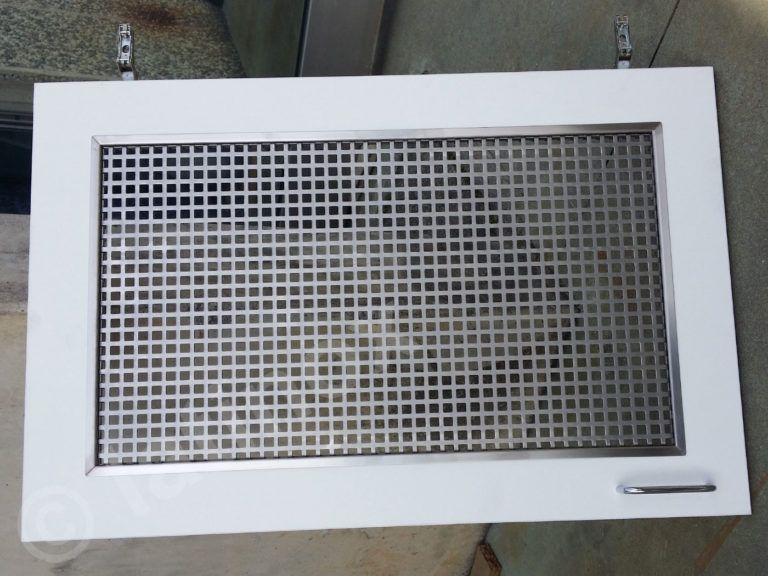 Copertura di ventilazione rettangolare bianca con griglia metallica, montata a parete.