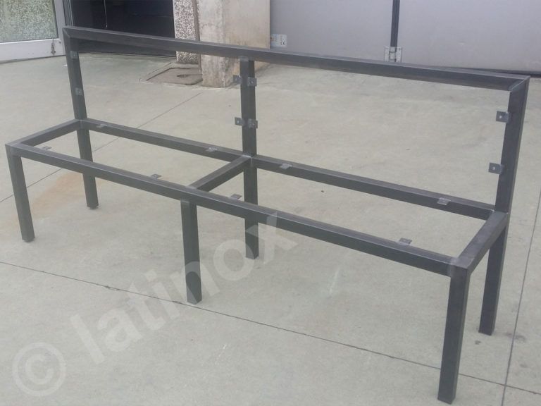 Panca con struttura in metallo, grigia, con schienale, posizionata all'esterno su una superficie in cemento.