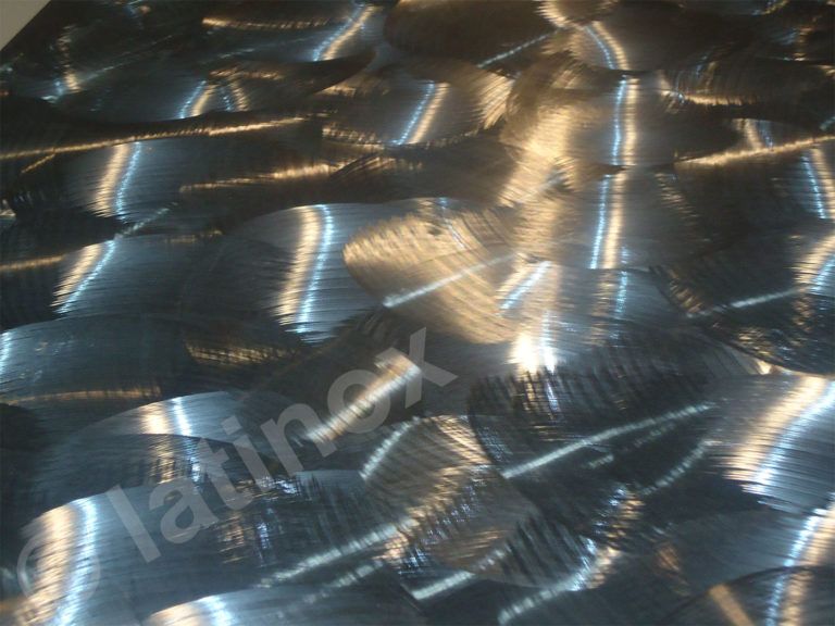 Superficie metallica strutturata con motivi sovrapposti e vorticosi che riflettono la luce.