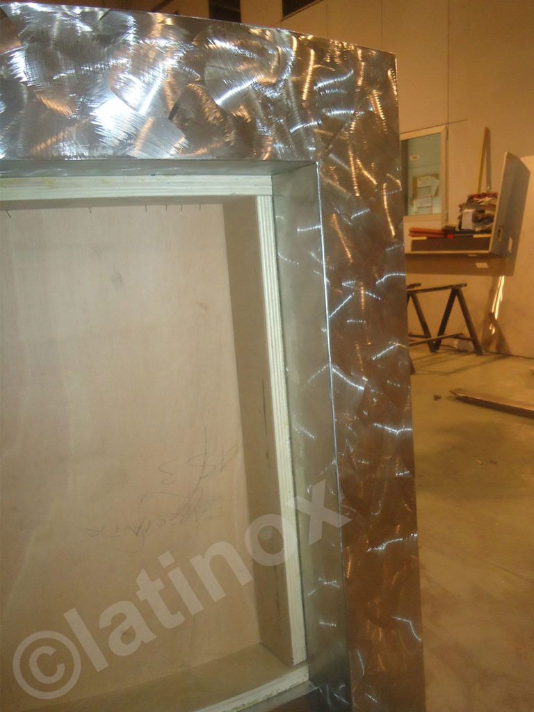 Telaio in lamiera di alluminio a forma di diamante che delimita una struttura in legno, probabilmente un telaio di una porta o di una finestra.