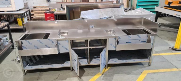 Bar in acciaio inox con lavelli, armadietti e postazione di lavoro. In un ambiente industriale.