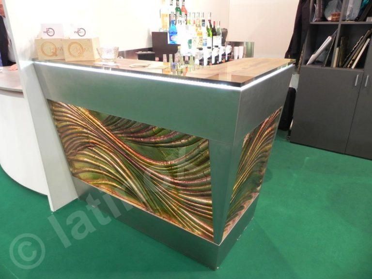 Bar moderno con design ondulato e colorato sulla facciata. Rifiniture argentate, bottiglie sul ripiano e pavimento verde.