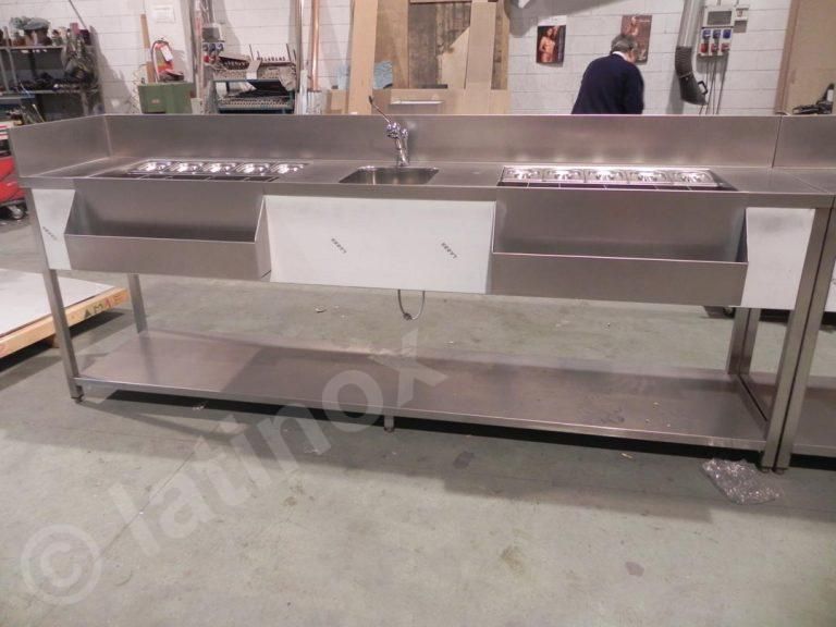 Bancone da cucina commerciale in acciaio inossidabile con piani cottura, lavello e spazio di archiviazione, con una persona sullo sfondo.