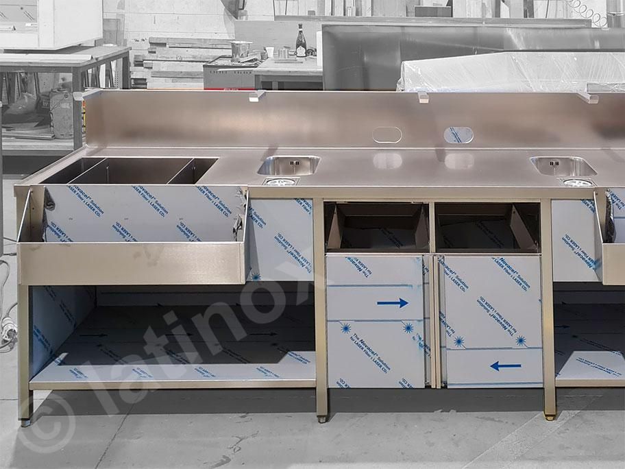 Bancone bar in acciaio inox con lavelli e vani portaoggetti.