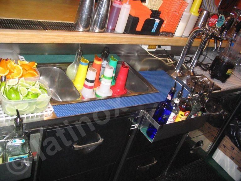 Bar con ingredienti e utensili, tra cui frutta, bottiglie e un lavandino.