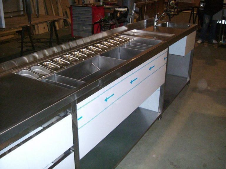 Bancone bar in acciaio inox con lavelli integrati, contenitori per alimenti e mobili contenitori bianchi.