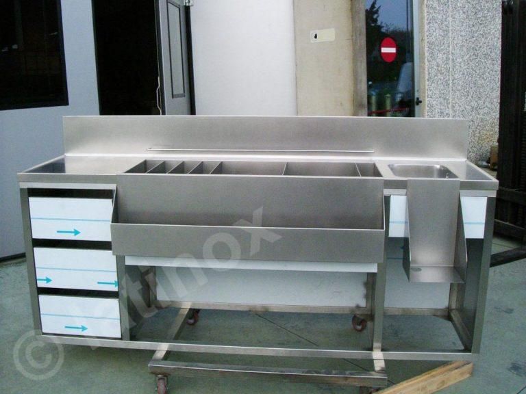 Bancone in acciaio inox con contenitori per il ghiaccio, cassetti e aree per la preparazione delle bevande.