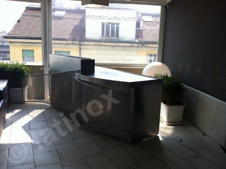 Bar all'aperto in acciaio inox su una terrazza piastrellata con piante in vaso e vista sulla città.