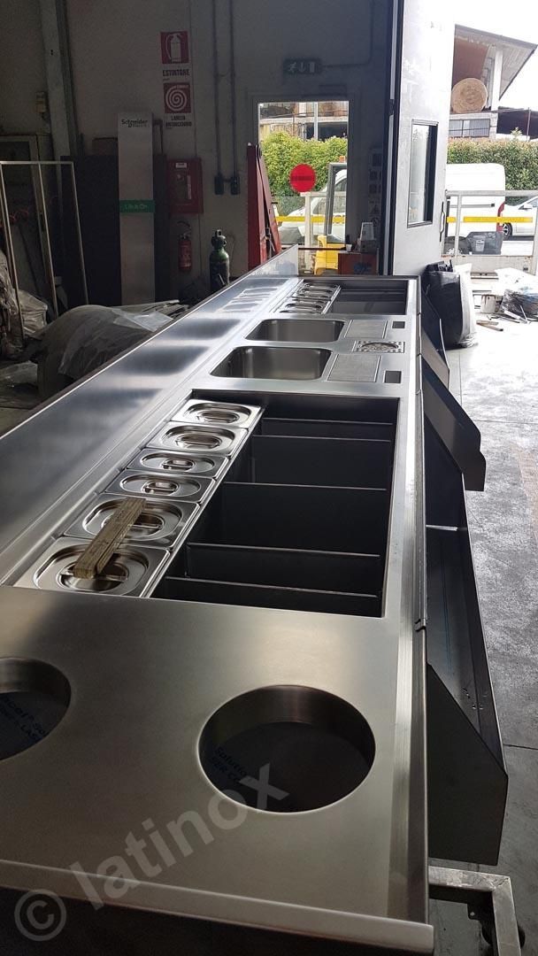 Piano di lavoro per cucina commerciale in acciaio inox con lavelli, fornelli e ritagli rotondi.