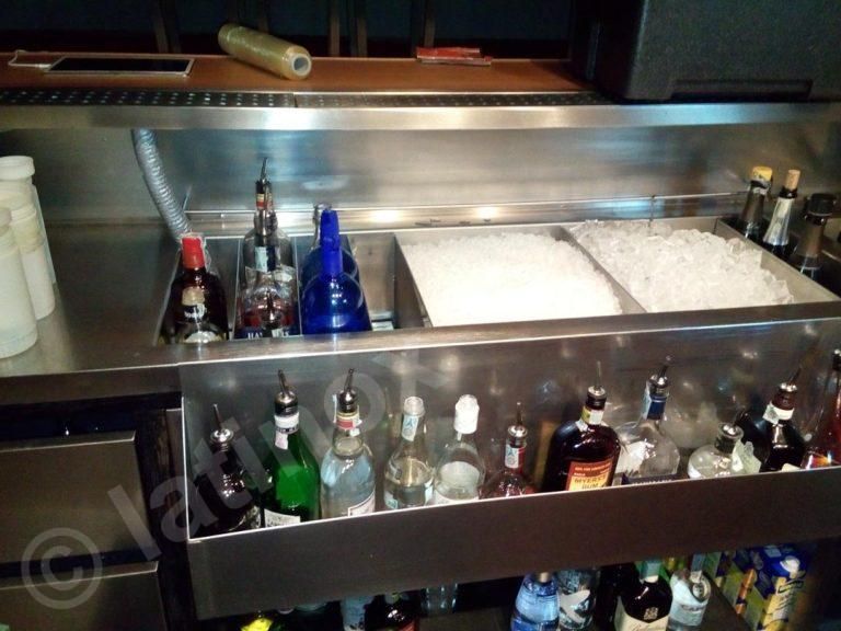 Bancone in acciaio inox con contenitori per il ghiaccio e bottiglie di liquore, pronto per la preparazione dei drink.