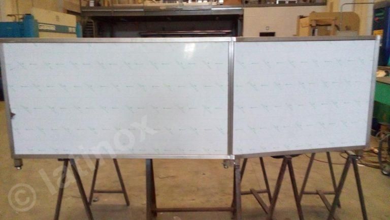 Due lavagne bianche con cornici metalliche su supporti a cavalletto in un'officina.