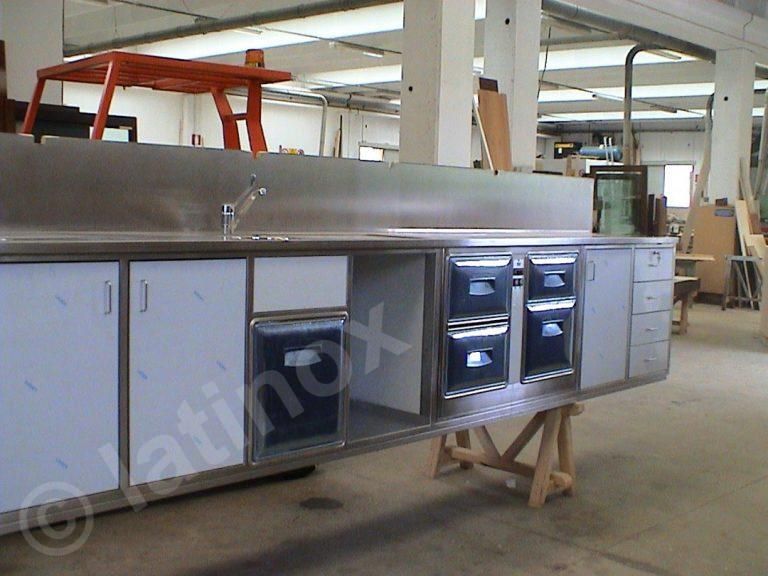 Bancone da cucina commerciale in acciaio inox con armadietti e cassetti, in un ambiente da officina.