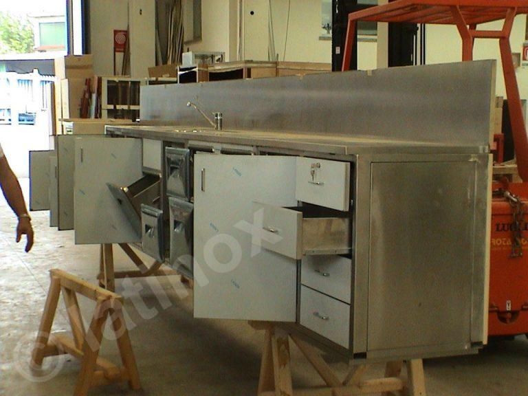 Mobile da cucina in acciaio inossidabile su cavalletti, con ante e cassetti aperti in un'officina.