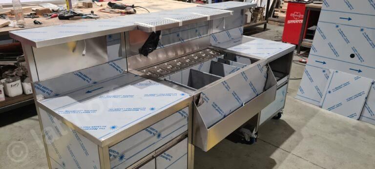 Bar in acciaio inossidabile con lavelli, spazio di stoccaggio e pellicola protettiva in un'officina.