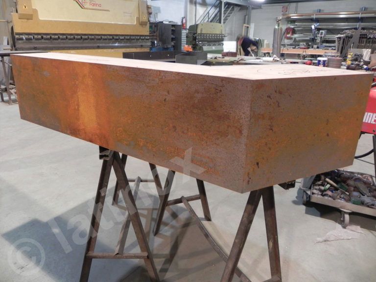 Grande blocco di metallo arrugginito su due cavalletti in un'officina.