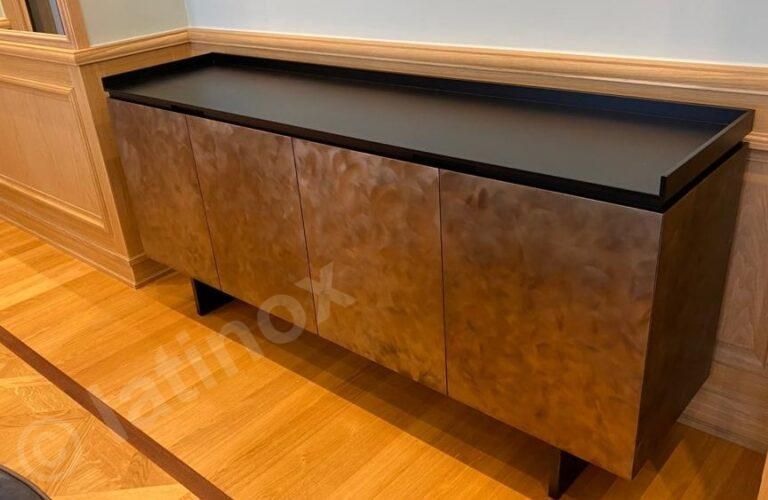 Mobiletto in legno marrone con piano e gambe neri su pavimento in legno.