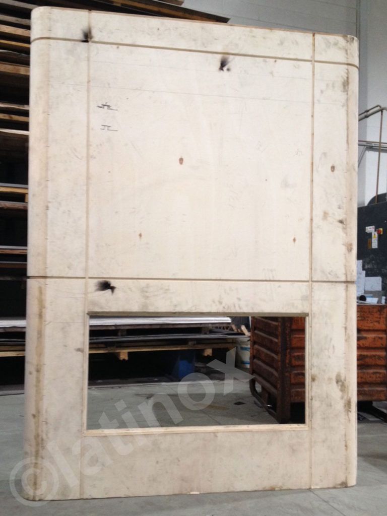 Grande pannello murale beige rettangolare con apertura rettangolare, che mostra segni di usura, in un'officina.